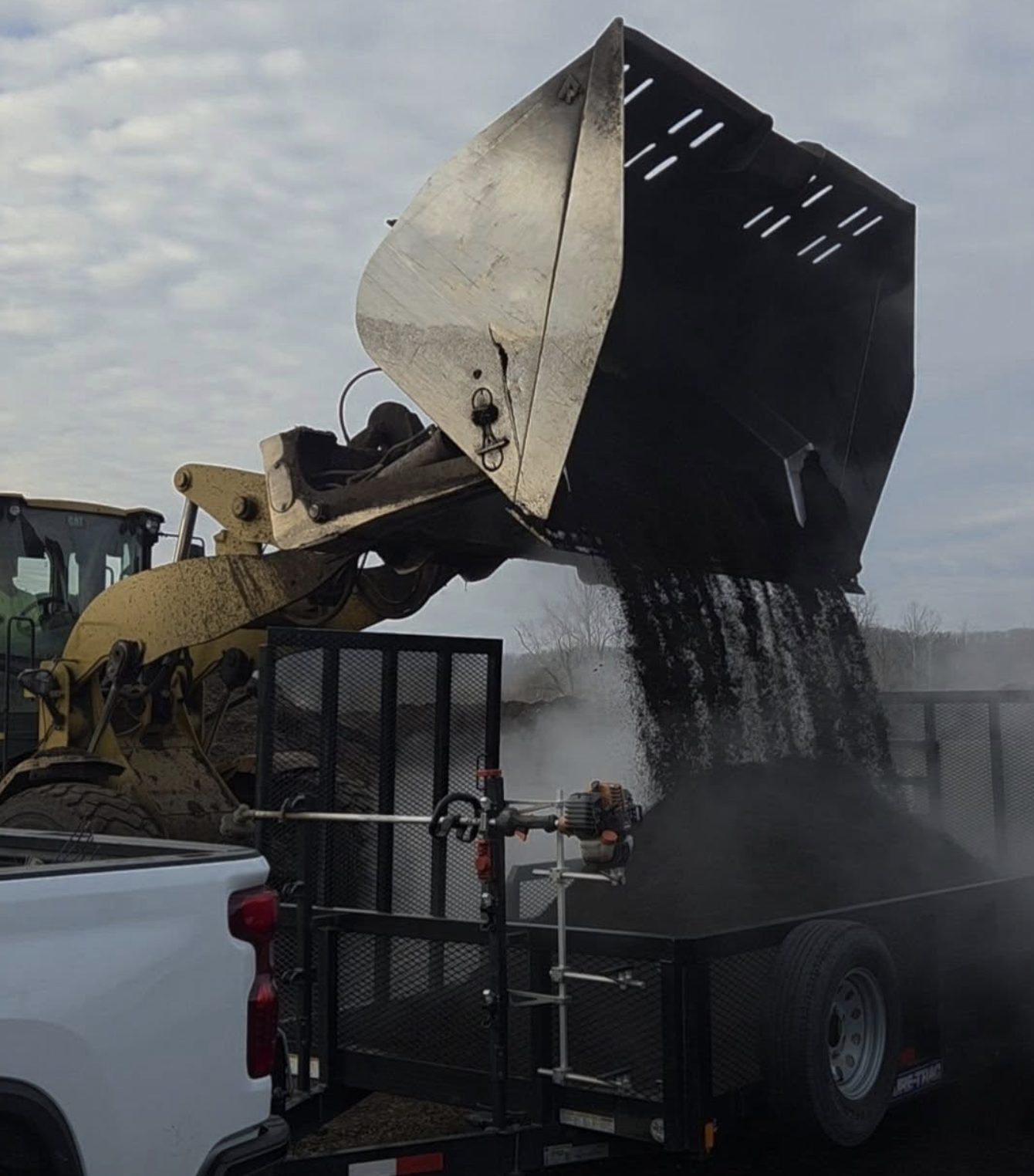 A loader dumping dark mulch into the Ewers trailer